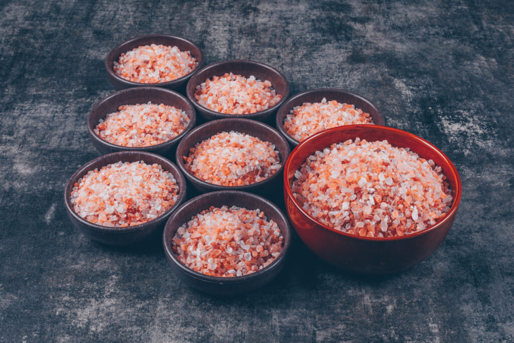 High angle view himalayan salt in big and small bowls on dark textured background. horizontal